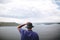 Hipster traveler in purple shirt  and bucket hat standing on top of rock mountain with amazing view on river. Young camper guy