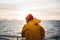Hipster traveler wearing red hat and yellow raincoat looking away at cloudy mountain and sunset sea