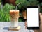 Hipster using smart phone with white blank screen taking photo of caramel macchiato coffee with stainless steel straw.