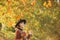 Hipster woman in vintage hat walking in park. Charming brunette in hat with autumnal leaves. Autumn queen wearing cozy
