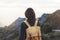 Hipster young girl with bright backpack enjoying sunset on peak of foggy mountain. Tourist traveler on background valley landscape