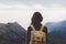 Hipster young girl with bright backpack enjoying sunset on peak of foggy mountain. Tourist traveler on background valley landscape