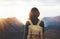 Hipster young girl with bright backpack enjoying sunset on peak of foggy mountain. Tourist traveler on background valley landscape