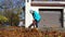 Hired female worker blowing leaves from garage entrance in autumn