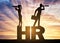 Hiring concept. A silhouette of a man and a woman stand on the letters HR and look through binoculars