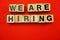 We are Hiring word created with cubes alphabet letters on red background