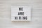`We are hiring` words on a modern board on a white wooden background, top view. Overhead, from above, flat lay. Close-up