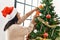 Hispanic brunette woman hanging christmas ball on tree at home