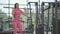 Hispanic brunette woman in a pink suit pushes a barbell over her head to the top while training her shoulders in the gym