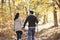 Hispanic couple hold hands hiking in forest, back view