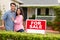 Hispanic couple satnding with a sign outside house