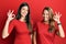 Hispanic family of mother and daughter wearing casual clothes over red background smiling positive doing ok sign with hand and