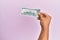 Hispanic hand holding 100 usa dollars banknote over isolated pink background