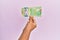 Hispanic hand holding 20 canadian dollars banknote over isolated pink background