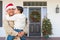 Hispanic Male Soldier Wearing Santa Cap Holding Mixed Race Son In Front of House