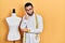 Hispanic man with beard dressmaker designer standing by manikin thinking looking tired and bored with depression problems with