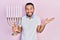 Hispanic man with beard holding menorah hanukkah jewish candle celebrating achievement with happy smile and winner expression with