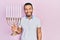 Hispanic man with beard holding menorah hanukkah jewish candle looking positive and happy standing and smiling with a confident