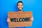 Hispanic man with beard holding welcome doormat smiling with a happy and cool smile on face