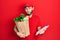 Hispanic man with beard wearing courier uniform with groceries from supermarket and clipboard clueless and confused expression