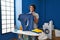 Hispanic man with curly hair ironing holding burned iron shirt at laundry room sticking tongue out happy with funny expression