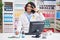 Hispanic man with curly hair working at pharmacy drugstore doing peace symbol with fingers over face, smiling cheerful showing