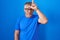 Hispanic man with grey hair standing over blue background making fun of people with fingers on forehead doing loser gesture