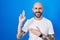 Hispanic man with tattoos standing over blue background smiling swearing with hand on chest and fingers up, making a loyalty
