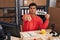 Hispanic man working at small business ecommerce holding open banner pointing with finger to the camera and to you, confident