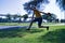 Hispanic mature adult man with a hat in hand jumping for joy on a park lawn on a sunny day