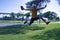 Hispanic mature adult man with a hat in hand jumping for joy on a park lawn on a sunny day