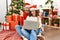 Hispanic middle age woman and mature man using laptop sitting by christmas tree smiling happy pointing with hand and finger to the