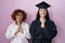 Hispanic mother and daughter wearing graduation cap and ceremony robe praying with hands together asking for forgiveness smiling