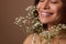 Hispanic pretty woman with closed eyes and beautiful smile, holding Gypsophila white sprig against beige background. Femininity,