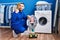 Hispanic repairman working on washing machine pointing thumb up to the side smiling happy with open mouth