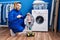 Hispanic repairman working on washing machine smiling happy pointing with hand and finger