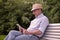 Hispanic senior man in summer hat reading tablet in park copy space