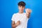 Hispanic teenager standing over blue background punching fist to fight, aggressive and angry attack, threat and violence