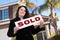 Hispanic Woman Holding Sold Sign In Front of House