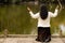 Hispanic Woman Kneeling in Prayer in Front of River in Forest Preserve