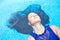 Hispanic woman with long black hair, floating back in the blue swimming pool