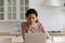 Hispanic woman sit in kitchen web surfing using laptop