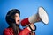 Hispanic woman wearing vintage motorbike helmet shouting angry on protest through megaphone