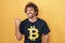 Hispanic young man wearing bitcoin t shirt smiling with happy face looking and pointing to the side with thumb up