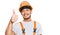 Hispanic young man wearing handyman uniform and safety hardhat smiling happy and positive, thumb up doing excellent and approval