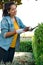 Hispanic young woman smiling and working on the yard cutting bush with hedge shear. Vertical photography