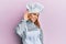 Hispanic young woman wearing professional cook uniform and hat smiling with hand over ear listening and hearing to rumor or gossip