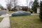 Historic antique muscle car in the driveway of a suburban house completely covered with a gray car protection cover.