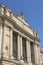 Historic building with large columns, blue sky, sculptures on the building