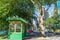 Historic green and yellow bus shelter building under London plane tree  in city street view with passing tram and urban skyline
